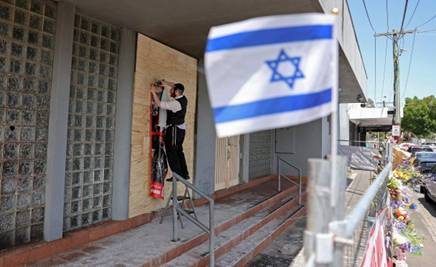 A member of the Jewish community staples a poster to the front of the damaged Adass Israel Synagogue in the Melbourne suburb of Ripponlea on December 9, 2024. Australian police said on December 9 they are hunting for three suspects linked to a Melbourne synagogue blaze, which authorities have designated as a terrorist act. (Photo by Martin KEEP / AFP)